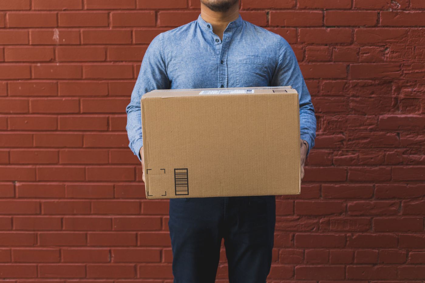A person holding a shipping box against a brick wall