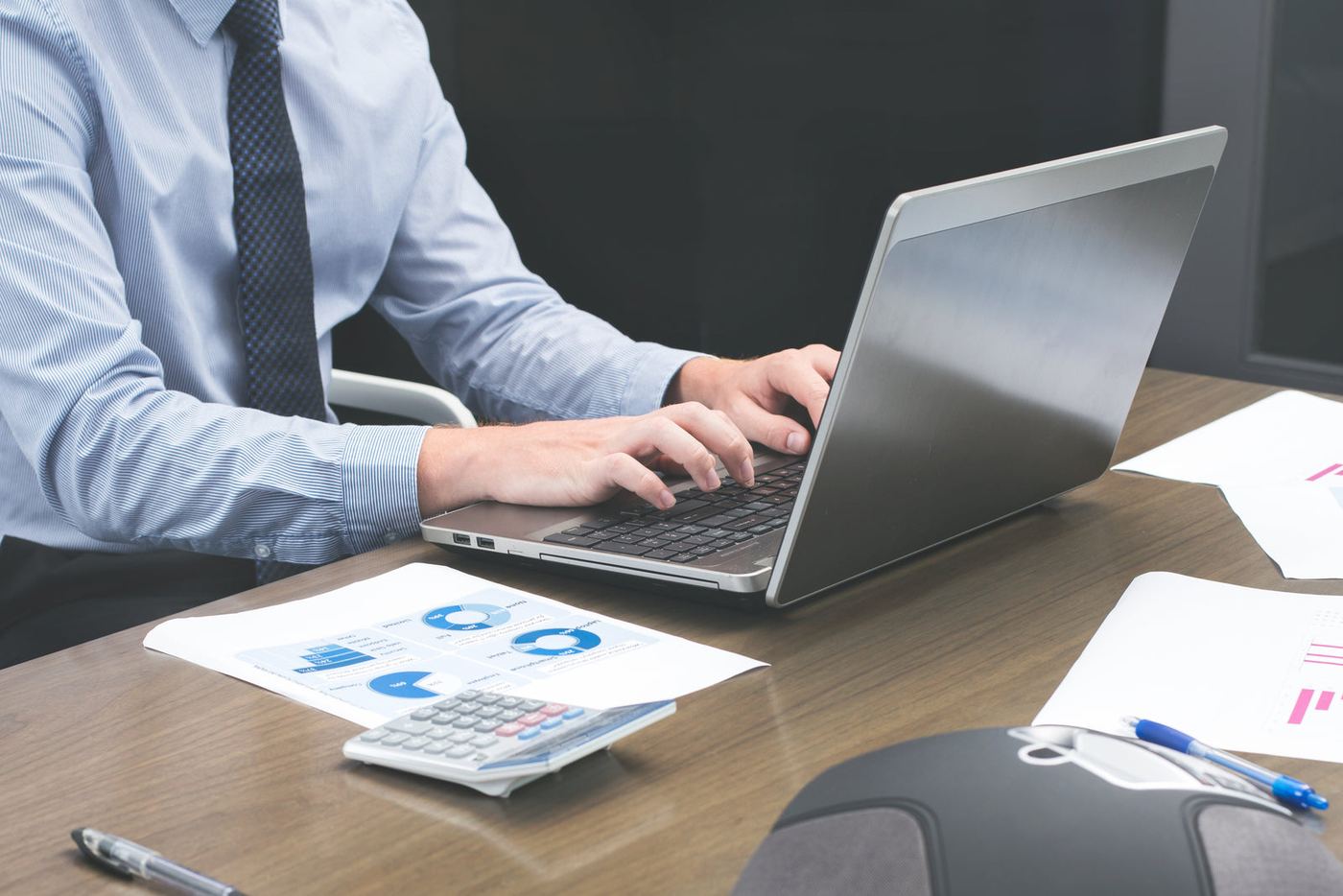 Someone working on a laptop with printed charts on the desk