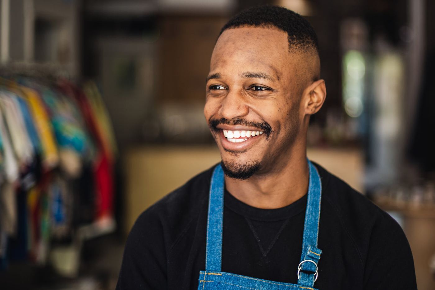 A smiling shop owner in an apron in his clothing store